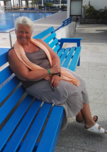 Kvinne sittende på en blå benk foran et utebasseng