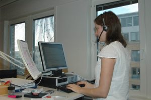 Kvinne står og jobber med headset og hjelpemidler ved arbeidsplassen
