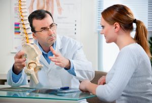 Lege viser pasient på en modell av en ryggrad