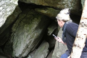 Dame som lyser inn i en mørk hule under store steiner