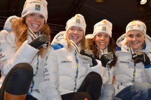 Fire kvinner sitter på huk og viser frem sølvmedaljen de har vunnet.