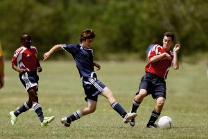 Tre unge gutter i fotballdrakter kjemper om en ball