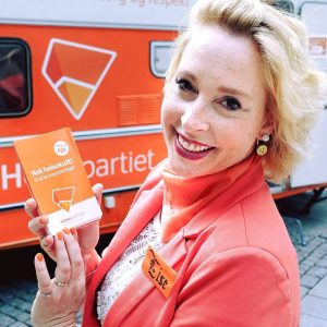 Lise Askvik med partiprogram foran en oransje campingvogn