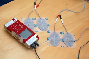 Rødt TENS-apparat med elektroder på et bord