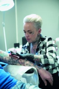 Kvinnlig tatovør tatoverer en arm på en kunde