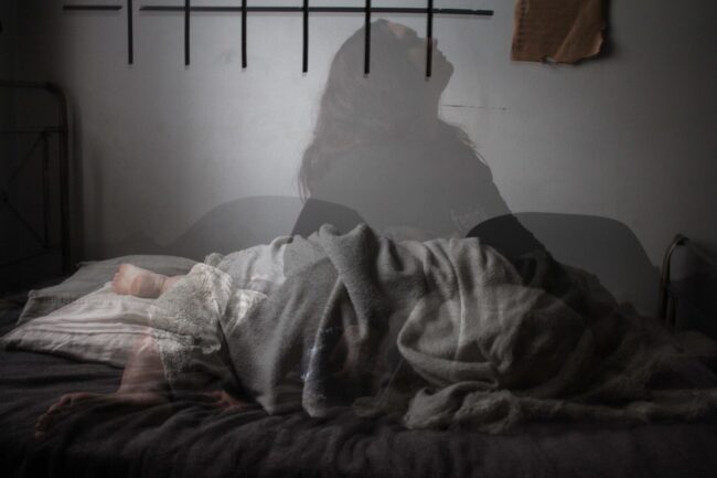 Bilde av skuggen til en kvinne som sitter i sengen og har vamskelig for å sove