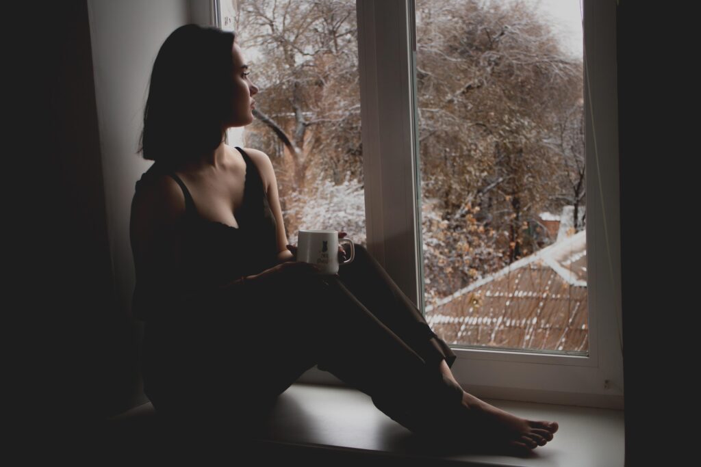 Ung kvinne sitter i vinduskarm og ser tenkende utover