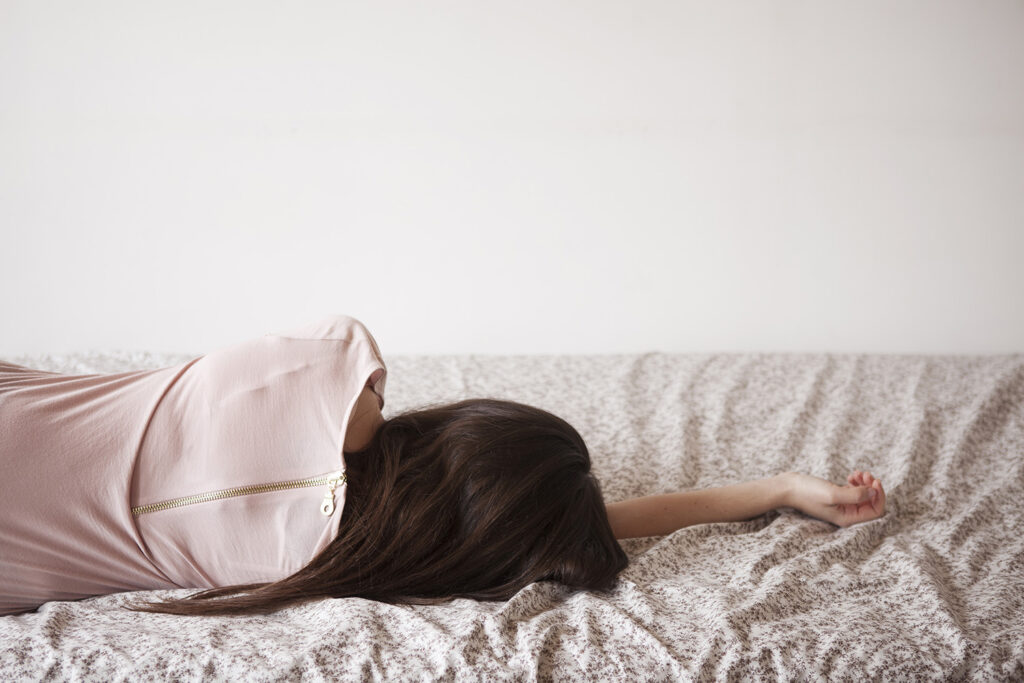 Kvinne ligger utmattet på sengen på grunn av fatigue