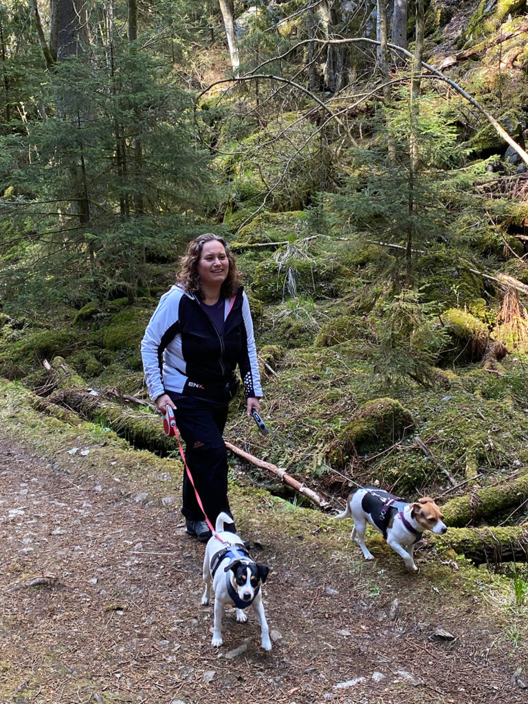 Kvinne går tur i skogen med to små hunder