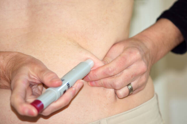 Kvinne setter penn med biologisk medisin subcutant, i underhuden.