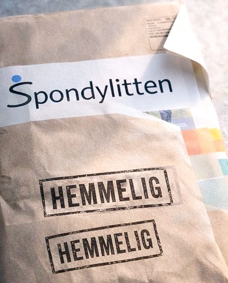 Deler av brun konvolutt med Logonavnet til Spondylitten og to stempler med 'Hemmelig' på. Langs den ene siden ser man et lite glimt av noen magasinsider