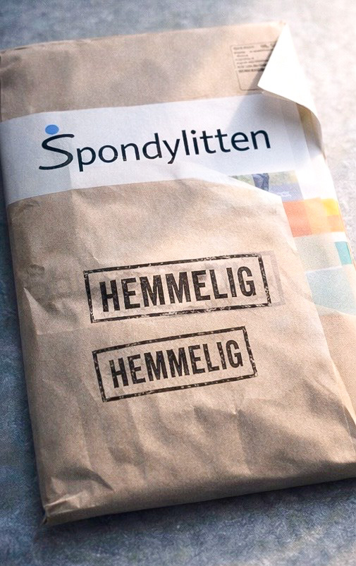 Brun konvolutt med Logonavnet til Spondylitten og to stempler med 'Hemmelig' på. Langs den ene siden ser man et lite glimt av noen magasinsider
