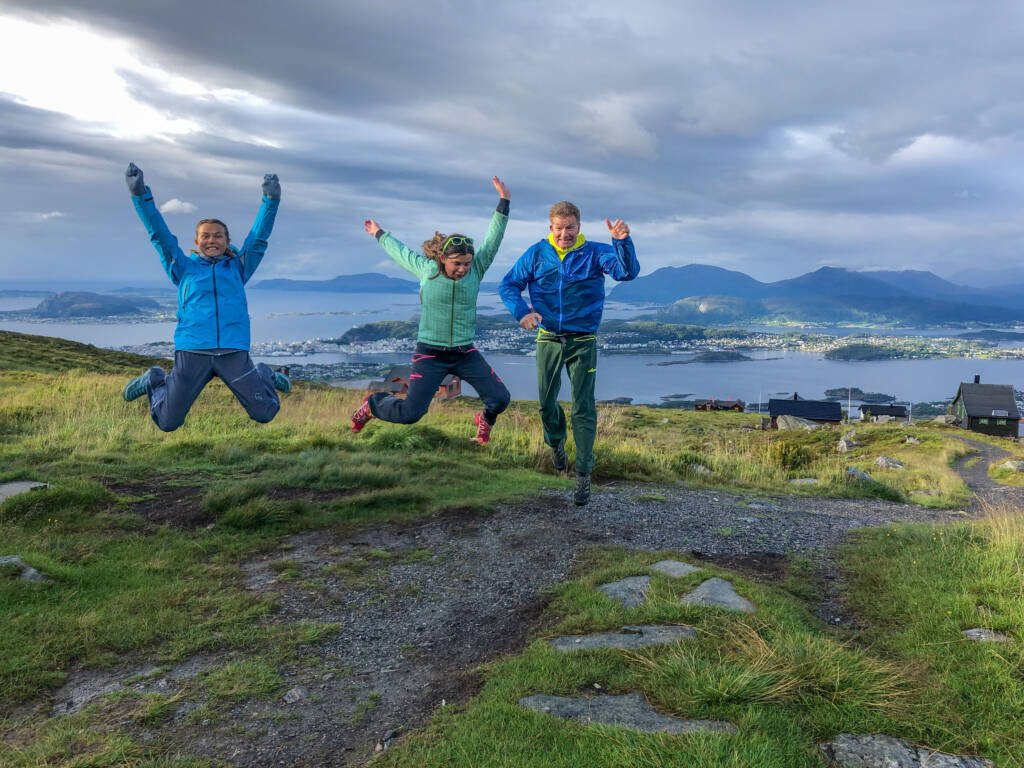 Tre hoppende glade turgåere på fjellet med idyllisk utsikt til fjorden bak
