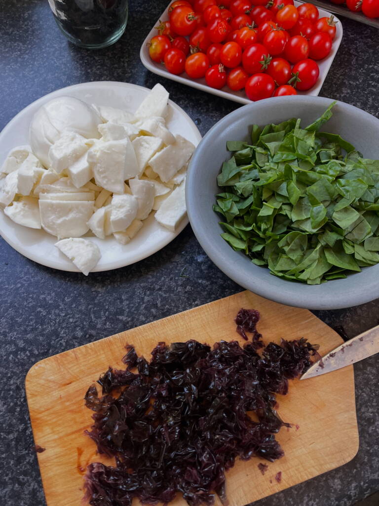 Fjøl med oppkuttet tare og skåler med annen pizzatopping som ost, cherrytomater og spinat