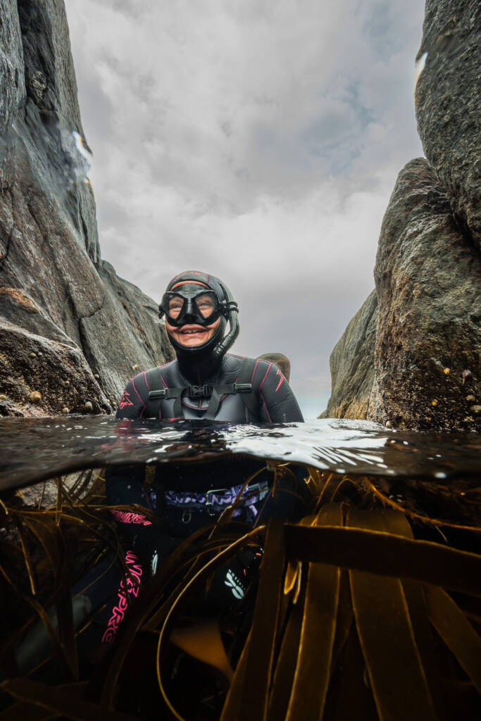 Spektakulært bilde av Melanie Endemann i fridykkerutstyr, tatt av Kristian Underwater. Han har fanget et øyeblikk med pur glede der hun er både over og under vann, med tareskog rundt seg