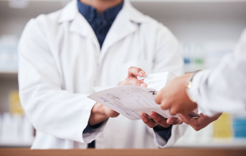 Hendene til farmasøyt gir medisiner og papirresept til hendene til en kunde